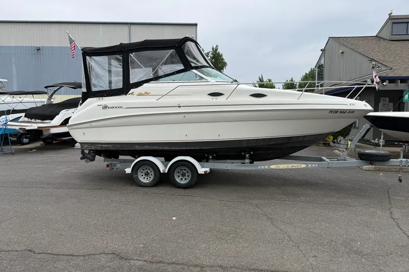 The Image of 1997 Sea Ray 240 Sundancer boat on trailer, parked outdoors near a building. - 0