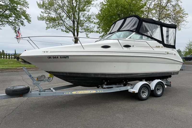 Slide: The Image of 1997 Sea Ray 240 Sundancer boat on trailer, parked outdoors with trees in background. - 4