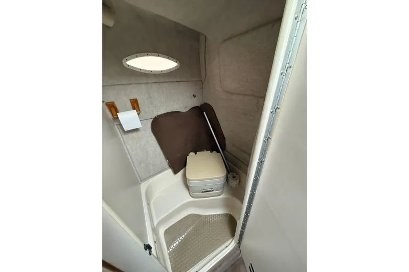 Slide: The Image of 1997 Sea Ray 240 Sundancer boat bathroom with compact toilet and porthole window. - 8
