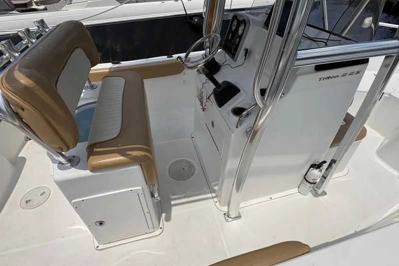 Slide: The Image of 2013 Seahunt Triton 225 boat seat with tan and white upholstery, cup holders, and water backdrop. - 15