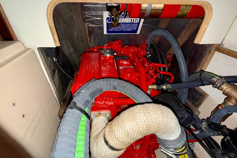 Slide: The Image of Engine compartment of a 1992 Island Packet 29 sailboat, featuring red engine and hoses. - 18