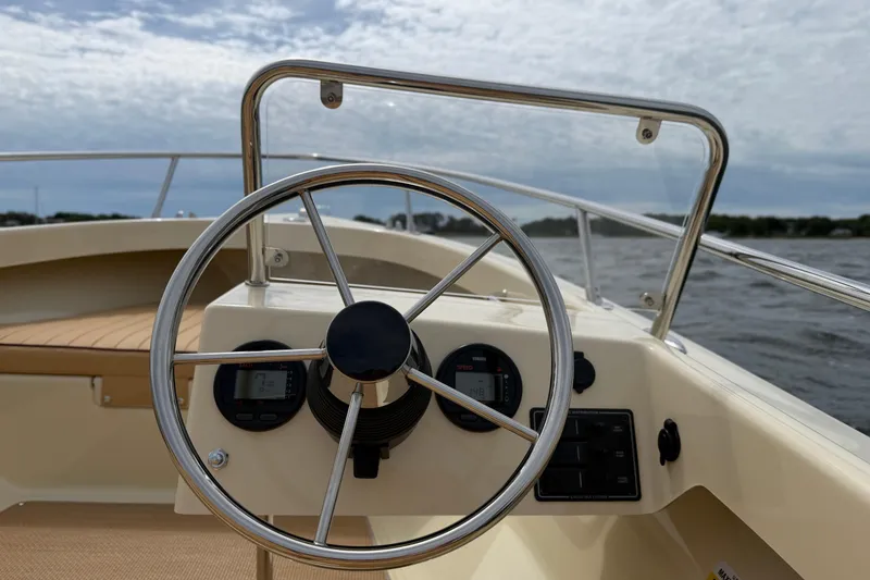 Slide: The Image of Steering wheel of 2027 Rossiter 14 boat with dashboard instruments, on a calm water backdrop. - 21