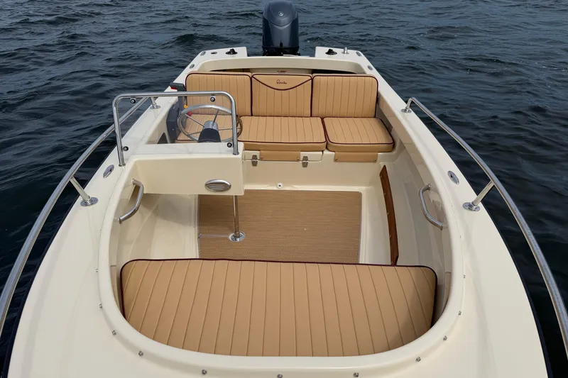 Slide: The Image of 2027 Rossiter 14 boat interior with tan seating, steering wheel, and open water backdrop. - 34