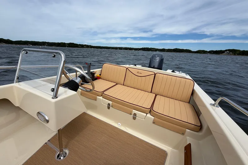 Slide: The Image of 2027 Rossiter 14 boat interior with tan cushioned seating on a calm lake. - 27