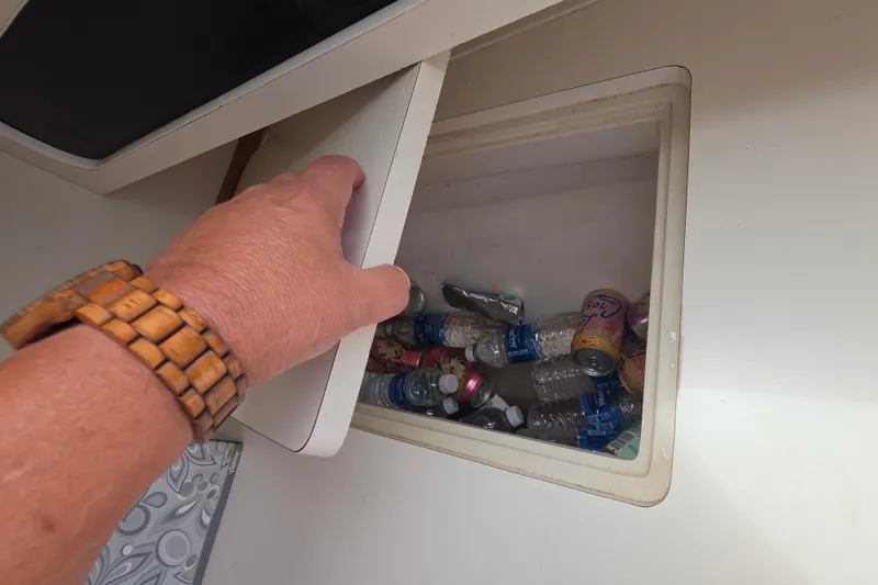Slide: The Image of Hand opening storage compartment on 1999 Catalina 270, revealing assorted bottles and cans. - 21