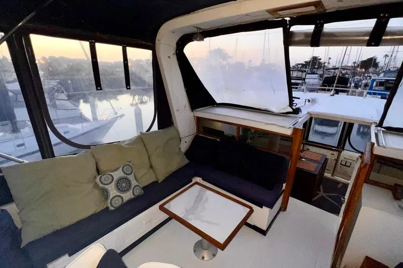 Slide: The Image of 1985 Heritage East 40 Sundeck interior with cozy seating and marina view at sunset. - 65