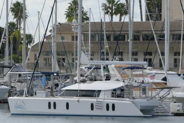Slide: The Image of 2014 Tayana Isara 50 yacht docked in a marina with palm trees in the background. - 104