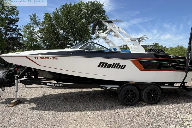 The Image of 2019 Malibu Wakesetter 24 MXZ boat on trailer, parked outdoors, with trees in background. - 0