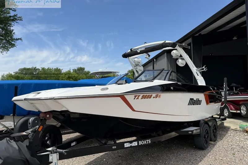 Slide: The Image of 2019 Malibu Wakesetter 24 MXZ boat on trailer, parked outdoors near a building. - 2