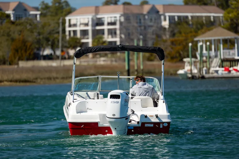 Slide: The Image of 2023 Hurricane SunDeck 187 OB boat cruising on a scenic waterway near residential buildings. - 4