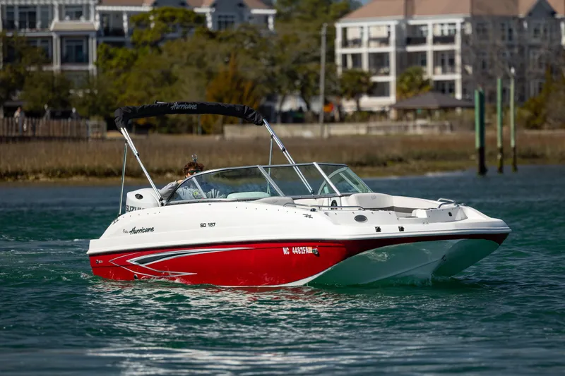 Slide: The Image of 2023 Hurricane SunDeck 187 OB boat cruising on a scenic waterway with buildings in the background. - 5