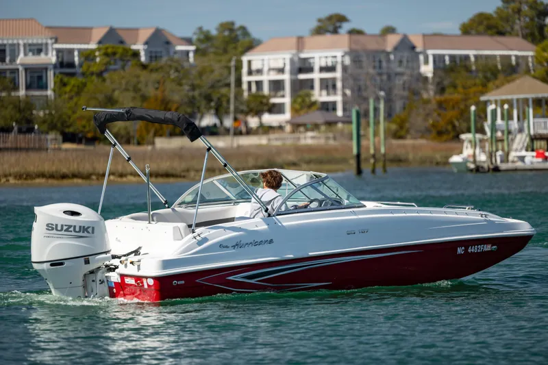 Slide: The Image of 2023 Hurricane SunDeck 187 OB boat cruising on a scenic waterway with buildings in the background. - 7