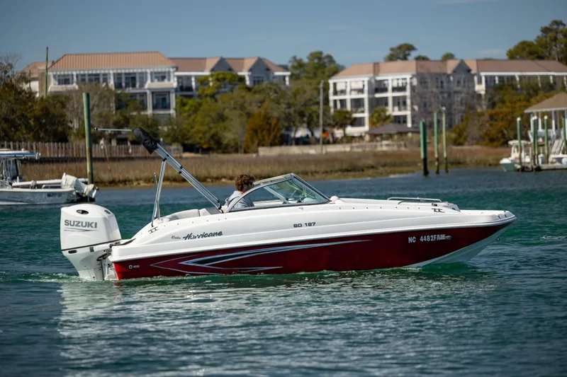 Slide: The Image of 2023 Hurricane SunDeck 187 OB boat cruising on a scenic waterway with buildings in the background. - 9