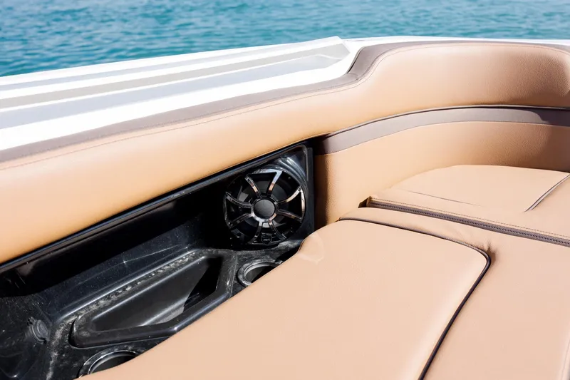 Slide: The Image of 2024 Yamaha Boats 275SD interior with tan seating and built-in speaker, near water. - 12
