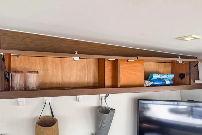 Slide: The Image of Open wooden cabinet in Lagoon 42 yacht, displaying glasses and cleaning supplies. - 42