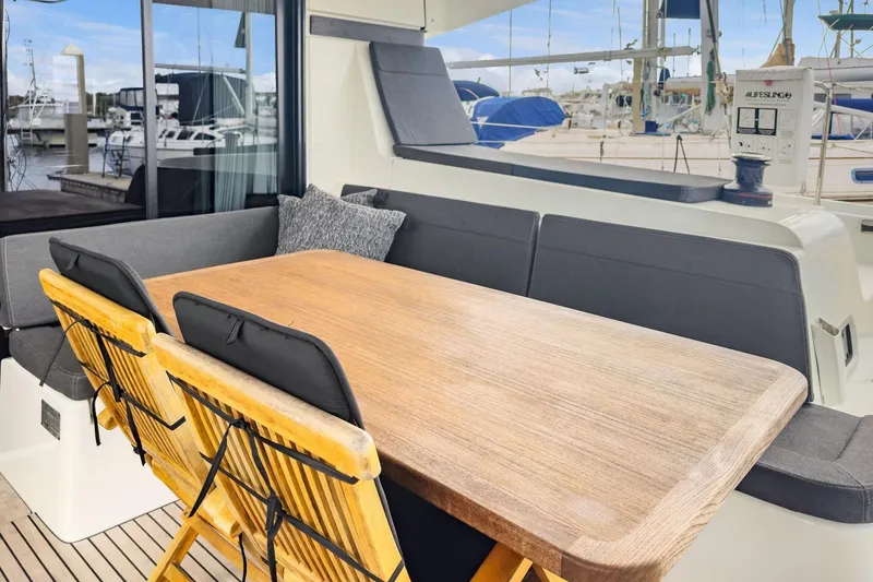 Slide: The Image of Outdoor seating area on 2020 Lagoon 42 catamaran with wooden table and cushioned chairs. - 7
