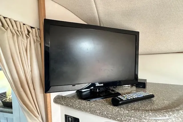 Slide: The Image of Flat-screen TV and remote on a countertop inside a 2001 Maxum 3000 SCR boat. - 29