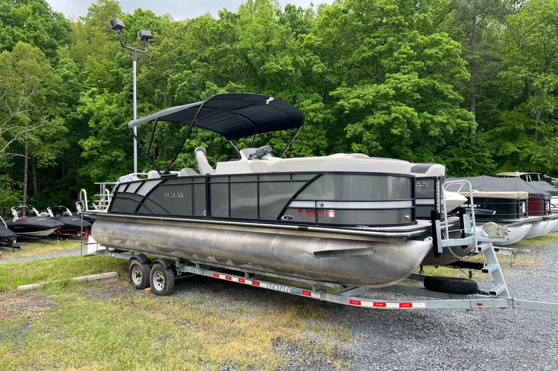 The Image of 2021 Sylvan L5 DLZ pontoon boat on trailer, surrounded by lush green trees. - 0