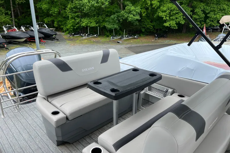 Slide: The Image of 2021 Sylvan L5 DLZ boat interior with seating and table, surrounded by lush greenery. - 12