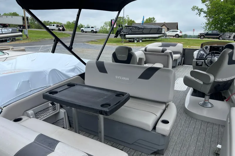 Slide: The Image of 2021 Sylvan L5 DLZ pontoon boat interior with seating and table, parked outdoors. - 13