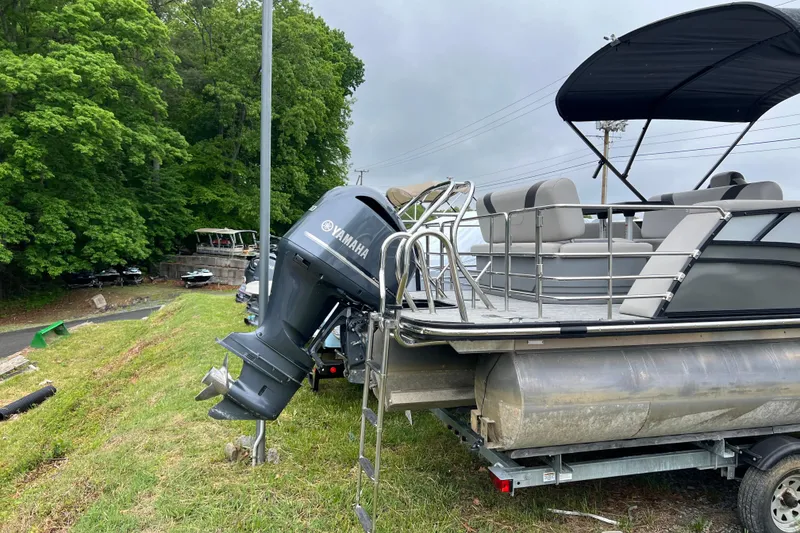 Slide: The Image of 2021 Sylvan L5 DLZ pontoon boat with Yamaha motor on a trailer, parked near lush greenery. - 2