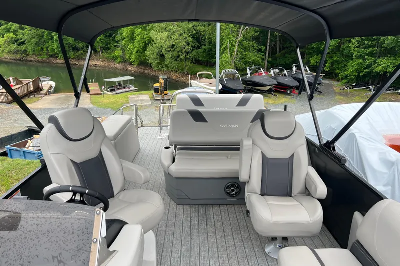 Slide: The Image of 2021 Sylvan L5 DLZ pontoon boat interior with plush seating, docked near a scenic lake. - 6