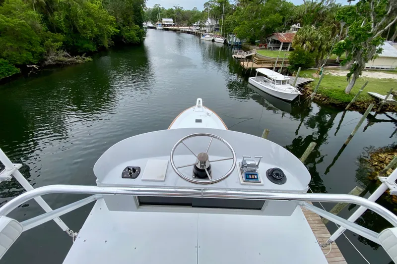 Slide: The Image of 1986 Huckins Sport Fisherman boat steering view on a serene river with lush greenery. - 10