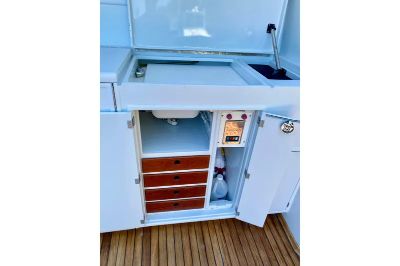 Slide: The Image of 1986 Huckins Sport Fisherman boat interior with open cabinet, drawers, and sink on wooden deck. - 13