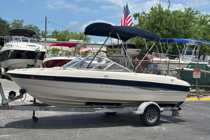 Slide: The Image of 2003 Bayliner 185 Capri boat on trailer, parked outdoors with American flag in background. - 10