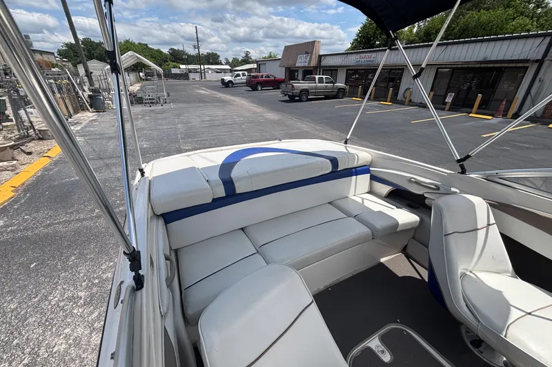 Slide: The Image of 2003 Bayliner 185 Capri boat interior with white seating, parked near shops. - 20