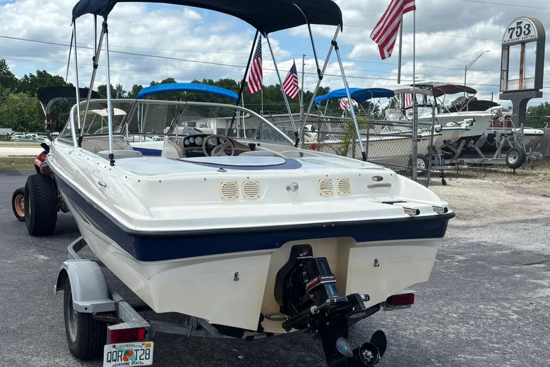Slide: The Image of 2003 Bayliner 185 Capri boat on trailer, American flags in background, outdoor dealership setting. - 3