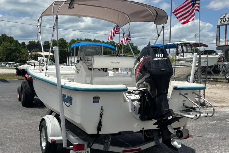 Slide: The Image of 2008 Sundance B18CC boat with Mercury 90 engine, parked on a trailer, American flags in background. - 2
