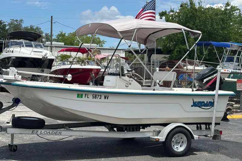 Slide: The Image of 2008 Sundance B18CC boat on trailer with canopy, parked outdoors, American flag in background. - 9