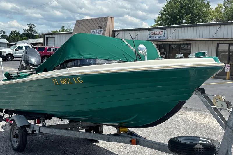 Slide: The Image of 1966 Mohawk 15 boat with green cover on trailer, parked outside marine store. - 13