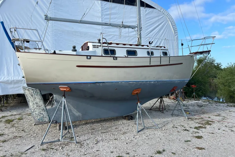 The Image of 1989 Pacific Seacraft Dana 24 sailboat on stands, outdoors under a clear sky. - 1