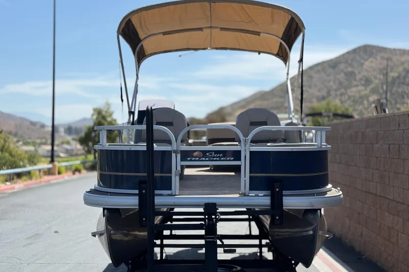 Slide: The Image of 2024 Sun Tracker Bass Buggy 18 DLX pontoon boat with canopy, parked on a sunny day. - 2