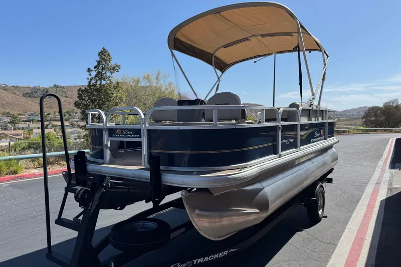 Slide: The Image of 2024 Sun Tracker Bass Buggy 18 DLX pontoon boat on trailer, parked outdoors. - 3