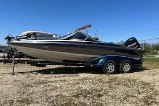 The Image of 2004 Ranger 210 Reata boat on trailer, parked outdoors under clear blue sky. - 0