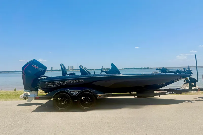 The Image of 2026 Nitro Z21 XL Pro boat on trailer by a lake under clear blue sky. - 0
