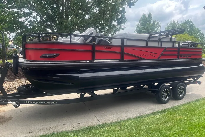 Slide: The Image of 2026 Ranger 220F pontoon boat on trailer, red and black design, parked outdoors. - 2