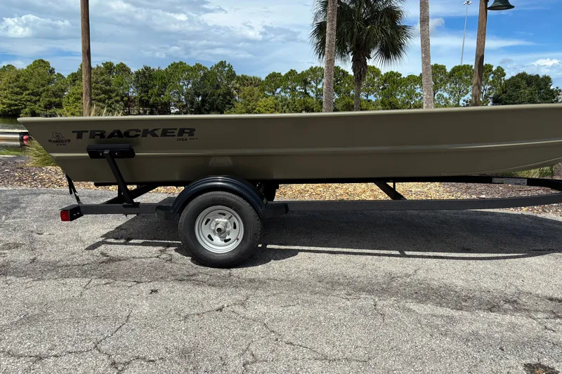 The Image of 2026 Tracker Grizzly 1754 Utility boat on trailer, parked outdoors with trees in background. - 0