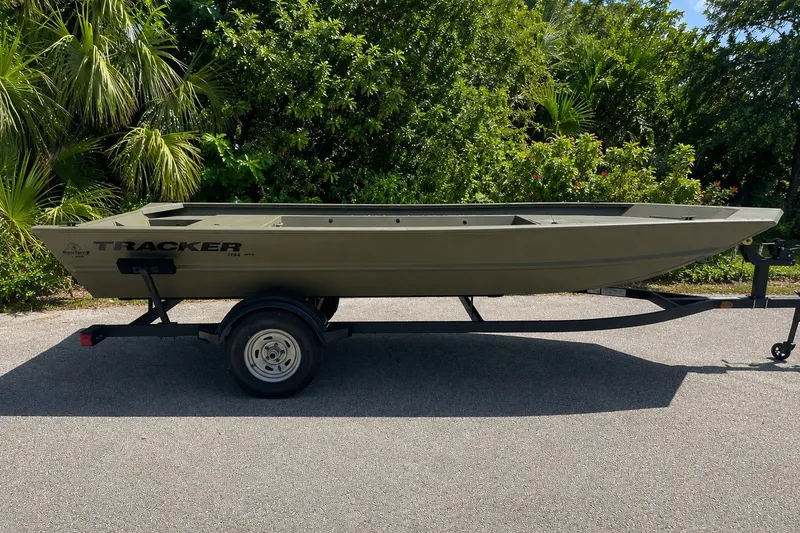 The Image of 2026 Tracker Grizzly 1754 Utility boat on trailer, surrounded by lush greenery. - 0