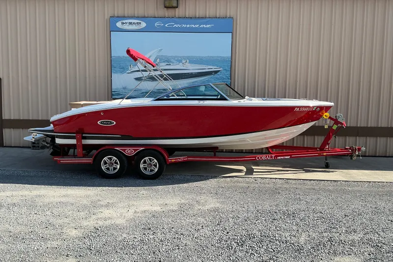 The Image of 2019 Cobalt CS23 boat in red on a matching trailer, parked outdoors. - 1