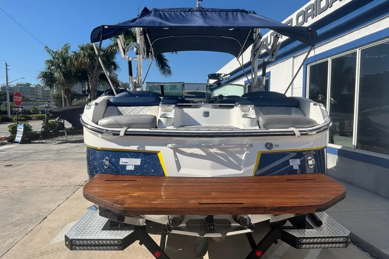Slide: The Image of 2015 MasterCraft X23 boat with blue canopy and wooden swim platform, parked outdoors. - 2