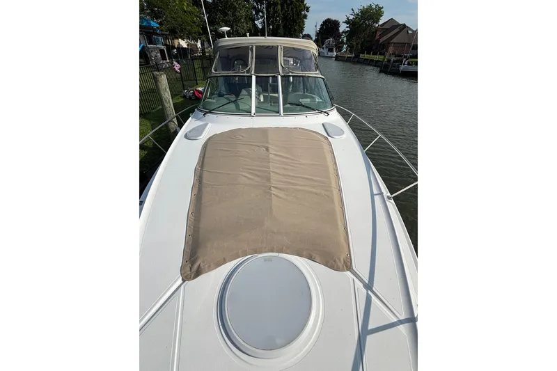 Slide: The Image of 2003 Cruisers Yachts 3470 Express boat with beige sunpad on deck, docked by a canal. - 27