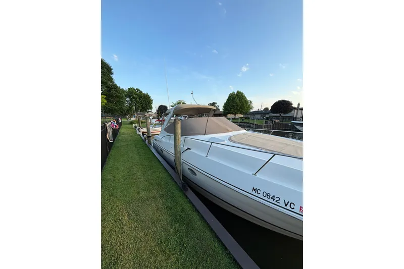 Slide: The Image of 2003 Cruisers Yachts 3470 Express docked by grassy shoreline under clear blue sky. - 4