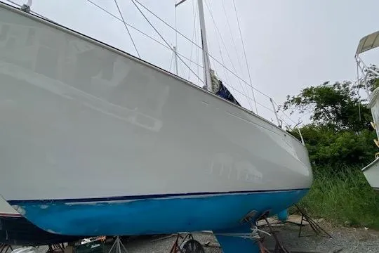 Slide: The Image of 1987 C&C Mark III sailboat on land, white hull with blue bottom, surrounded by greenery. - 16