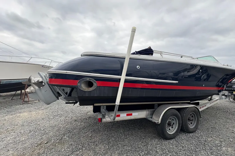 Slide: The Image of 2002 Chris-Craft Launch 28 boat on trailer, dark blue with red stripe, overcast sky. - 16