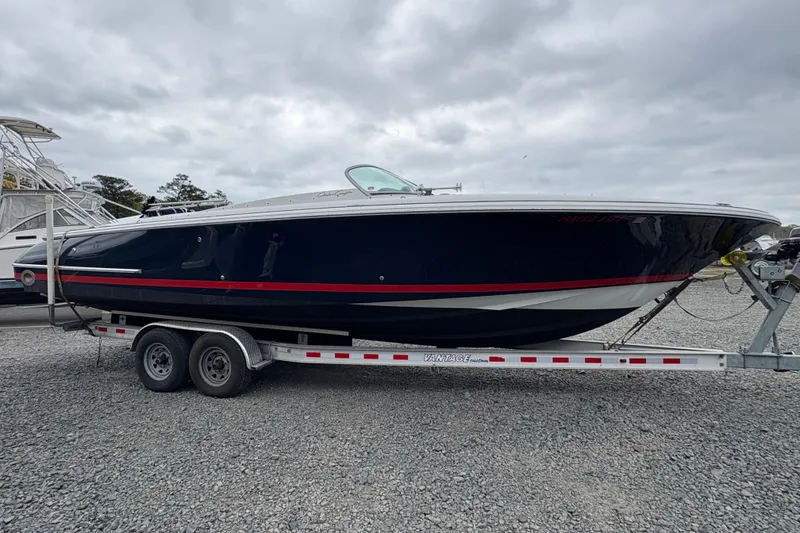 Slide: The Image of 2002 Chris-Craft Launch 28 boat on trailer, parked on gravel under cloudy sky. - 20