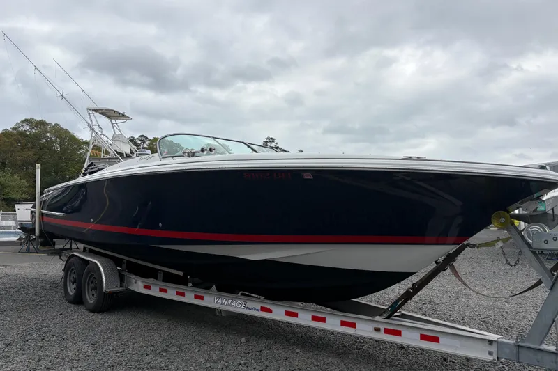 Slide: The Image of 2002 Chris-Craft Launch 28 boat on trailer, dark hull with red stripe, overcast sky. - 21
